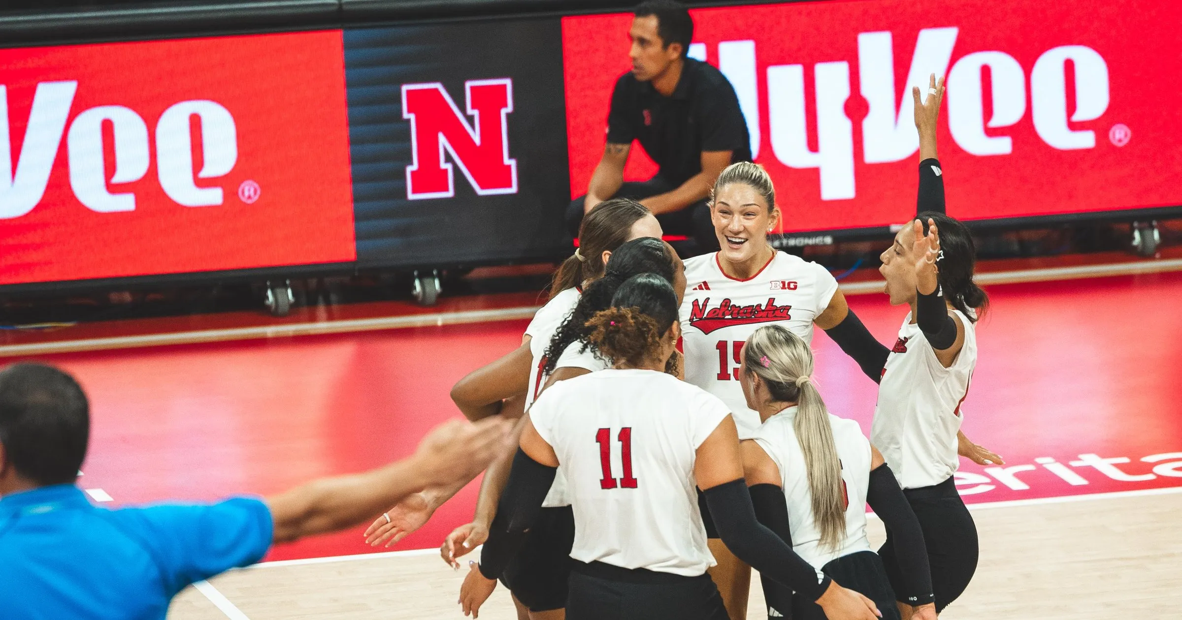Andi Jackson (15) smiles in the middle of a Nebraska huddle during the Georgia Tech match, with Teraya Sigler (11) in the foreground and a teammate raising her arm behind them.