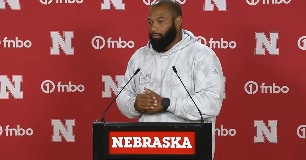 EJ Barthel speaking at a podium marked Nebraska, in a white Huskers Football hoodie, in front of a red backdrop.