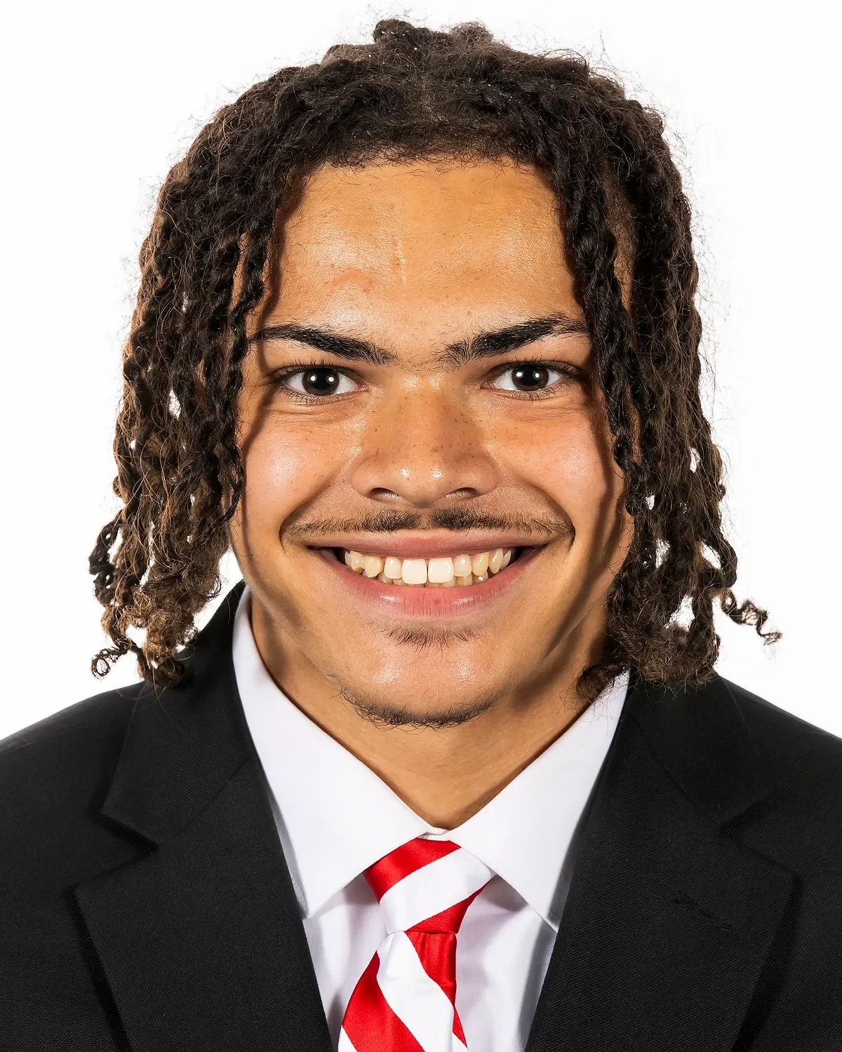 Mekhi Nelson in a dark suit and red-striped tie, photographed against a white background.