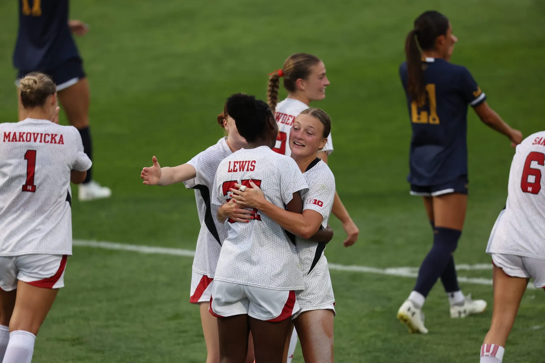 Nathalie Lewis is embraced by a teammate on the field at Hibner Stadium as other Nebraska players run in to celebrate.
