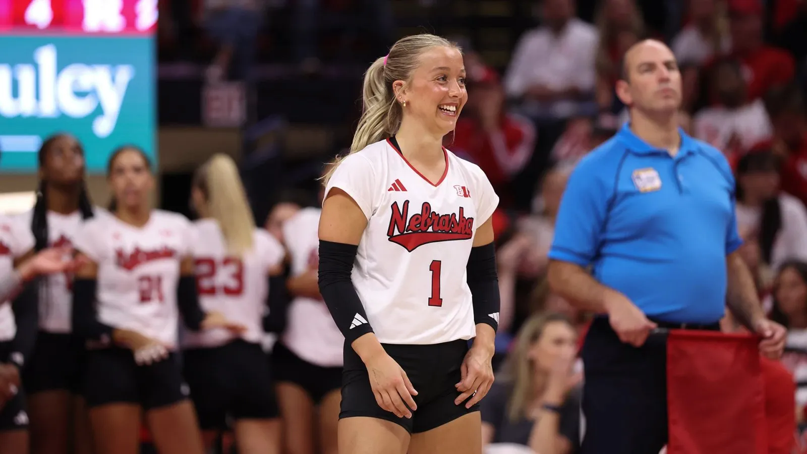 Keri Leimbach (1) smiles on the court at John Cook Arena during Nebraska's Big Ten opener against Rutgers, teammates and an official behind her.