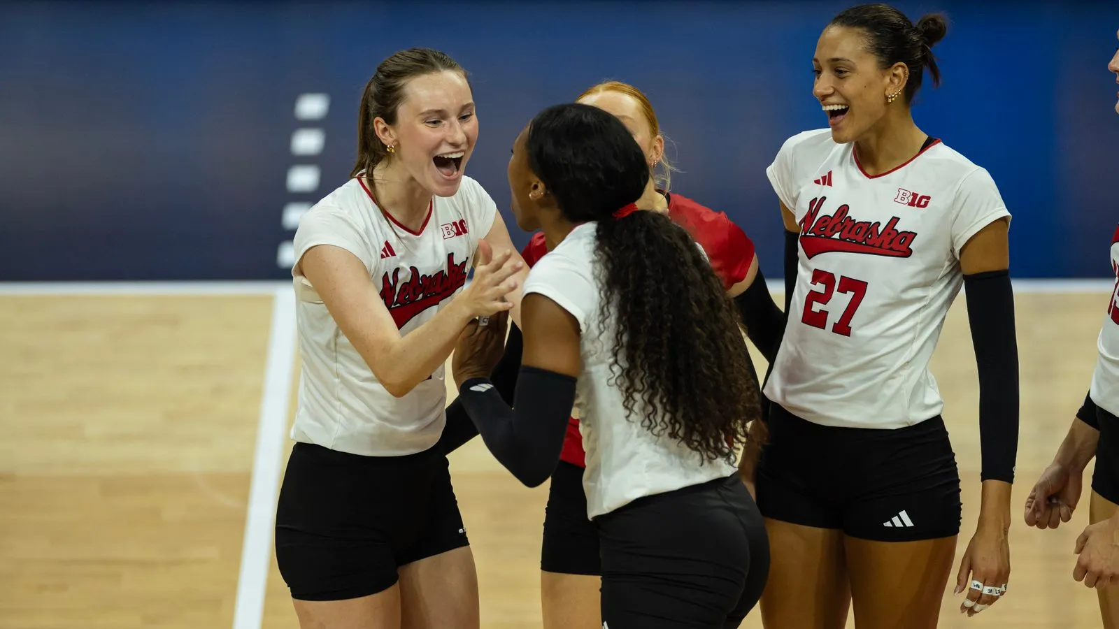 Nebraska volleyball players celebrate a point against North Carolina, Harper Murray (27) smiling at right as teammates slap hands.