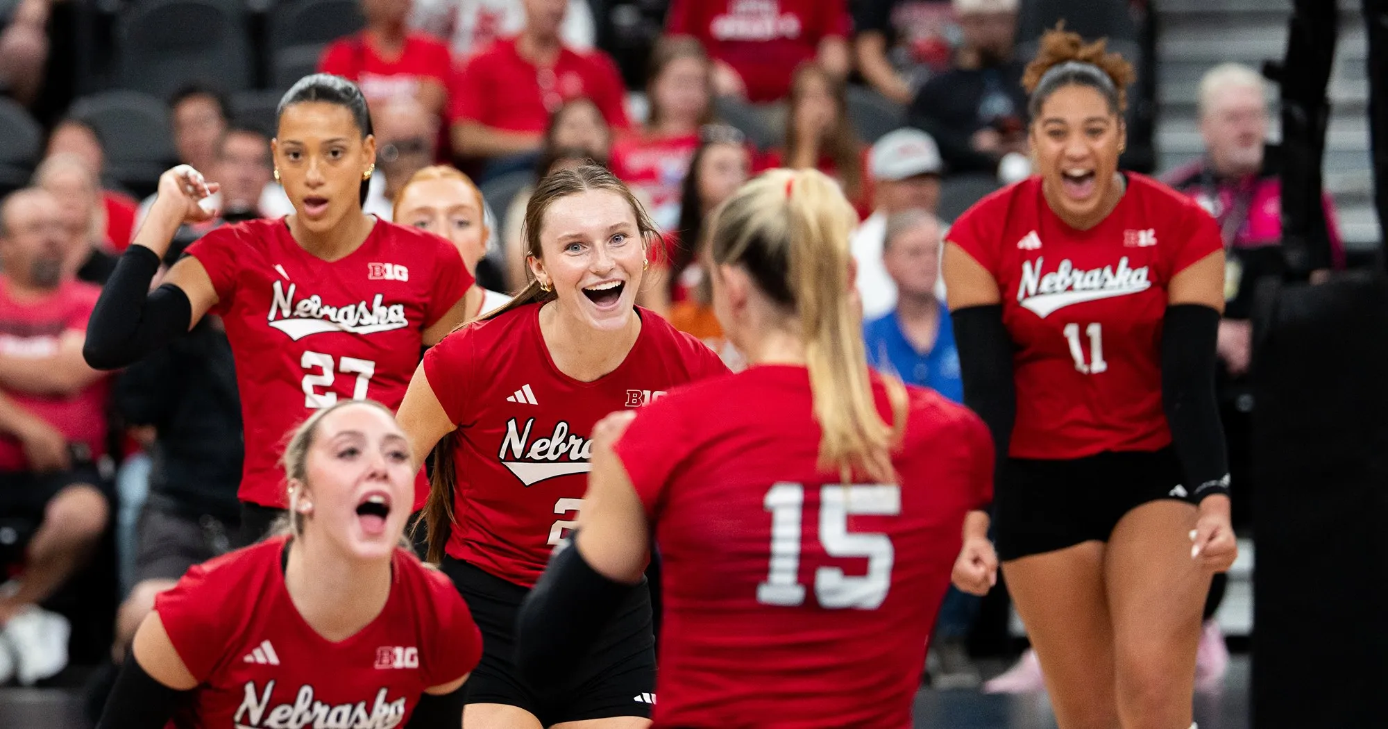 Nebraska volleyball players in red celebrating a point at T-Mobile Arena, with Harper Murray (27) and Teraya Sigler (11) shouting and Andi Jackson (15) facing away from the camera.