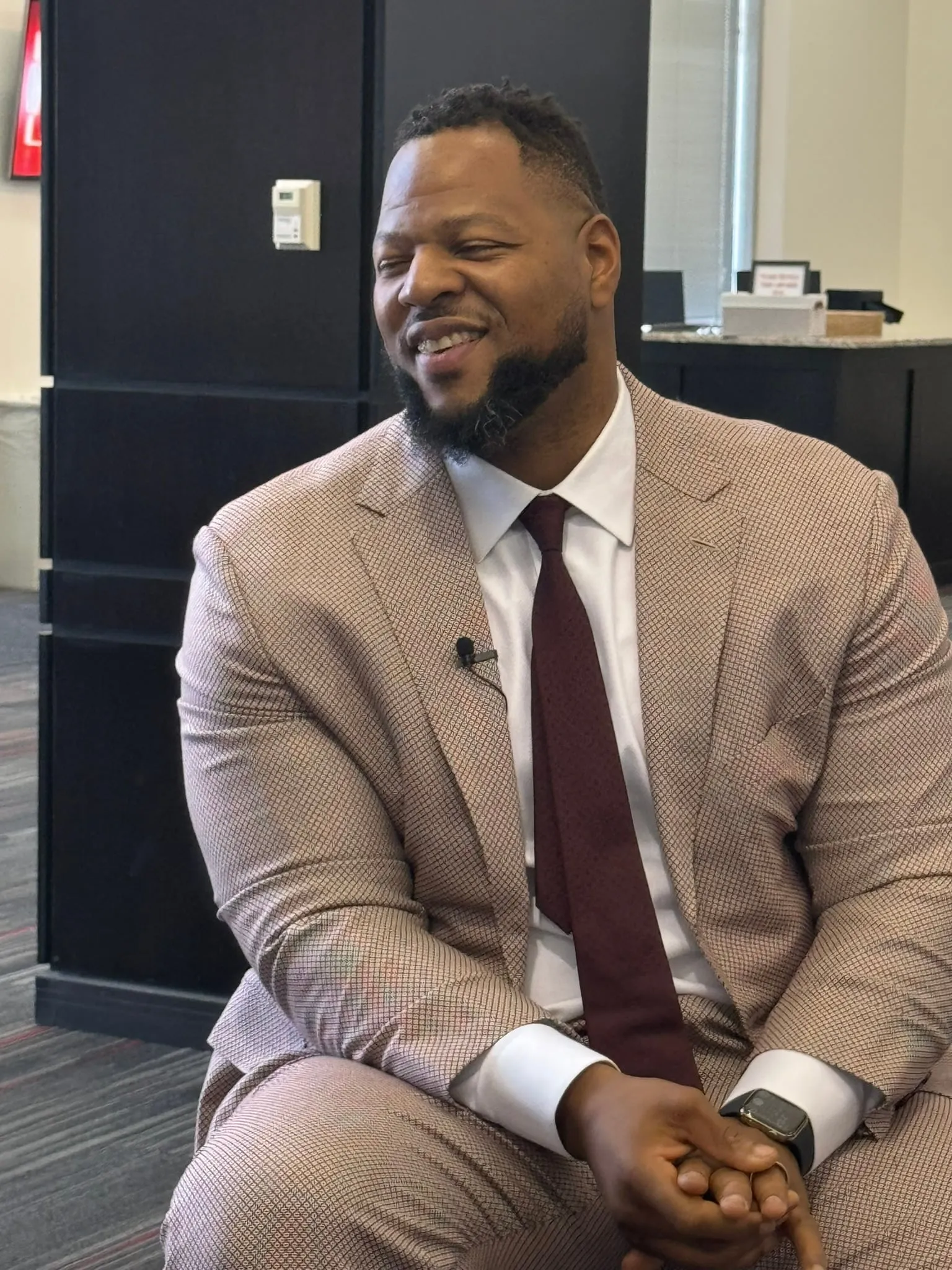 Ndamukong Suh, seated in a tan suit with a lapel microphone, smiles during an interview on the night of his Hall of Fame induction.